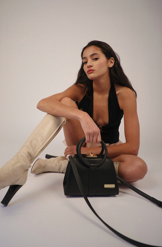 long dark haired girl with white boots sitting holding black kaila katherine bloomsbury vegan leather handbag